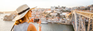Young woman tourist photographing with phone beautiful landscape view on the old town with river and famous iron bridge in Porto city, Portugal
