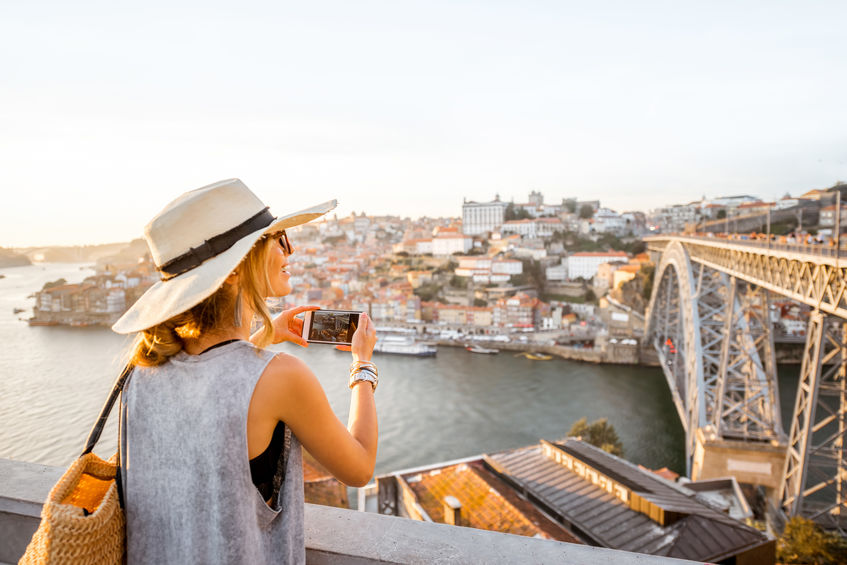 Young woman tourist photographing with phone beautiful landscape view on the old town with river and famous iron bridge in Porto city, Portugal