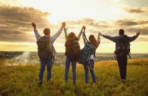 Happy people tourists stand raised their hands up at sunset on the nature.