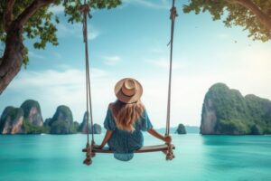A young girl swings on a swing on the coast near palm trees.